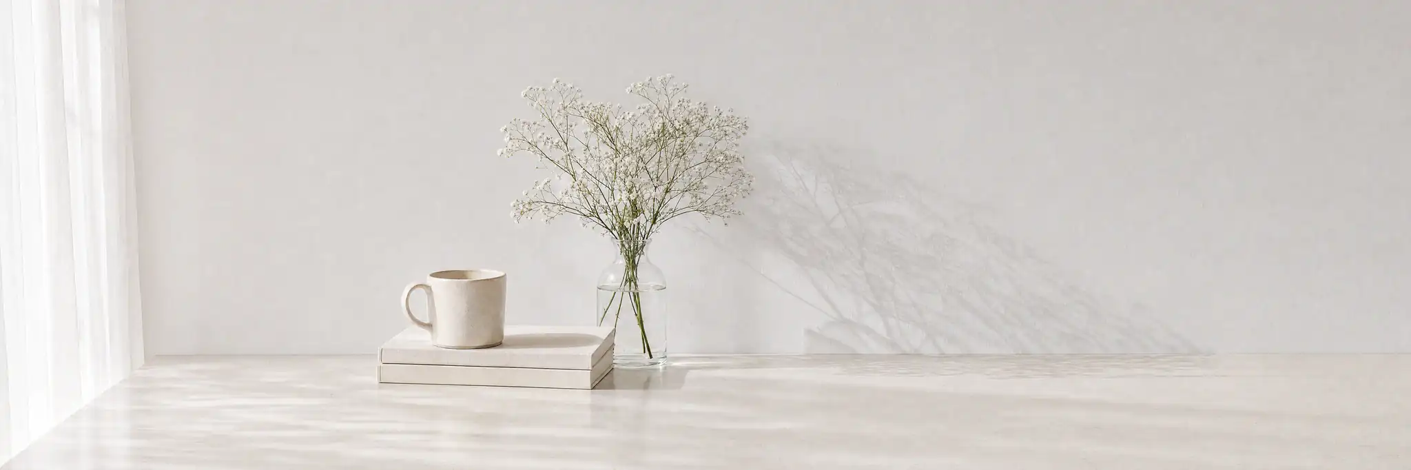 Objects on a sunlit white table with flower shadows cast across the wall